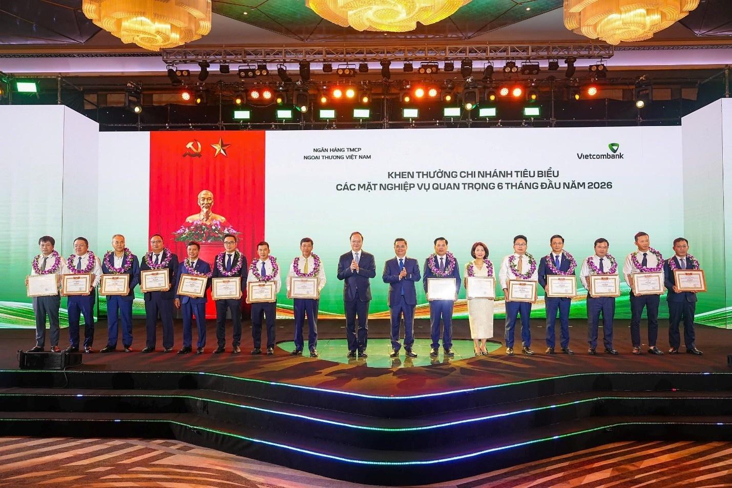  Đồng chí Nguyễn Thanh Tùng - Bí thư Đảng ủy, Chủ tịch HĐQT Vietcombank (thứ 8 từ phải sang) tặng giấy khen và đồng chí Lê Quang Vinh - Phó Bí thư Đảng ủy, Thành viên HĐQT, Tổng Giám đốc Vietcombank (thứ 9 từ phải sang) trao hoa chúc mừng cho 15 chi nhánh tiêu biểu trong hoạt động kinh doanh 6 tháng đầu năm 2026. 
