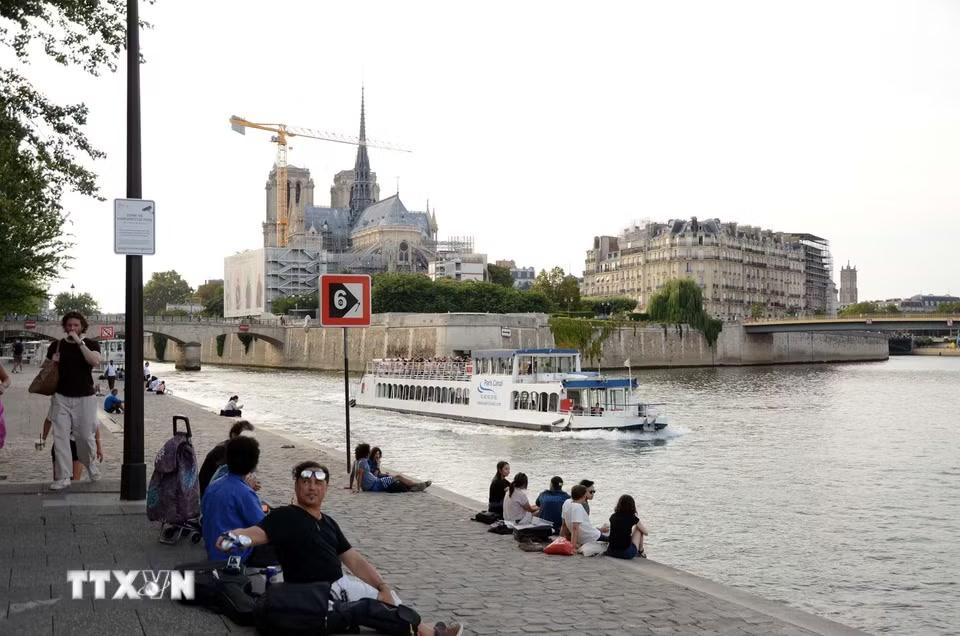 Người dân và du khách ngồi thư giãn bên bờ sông Seine, phía xa là Nhà thờ Đức Bà Paris. (Ảnh: Hữu Chiến/TTXVN)