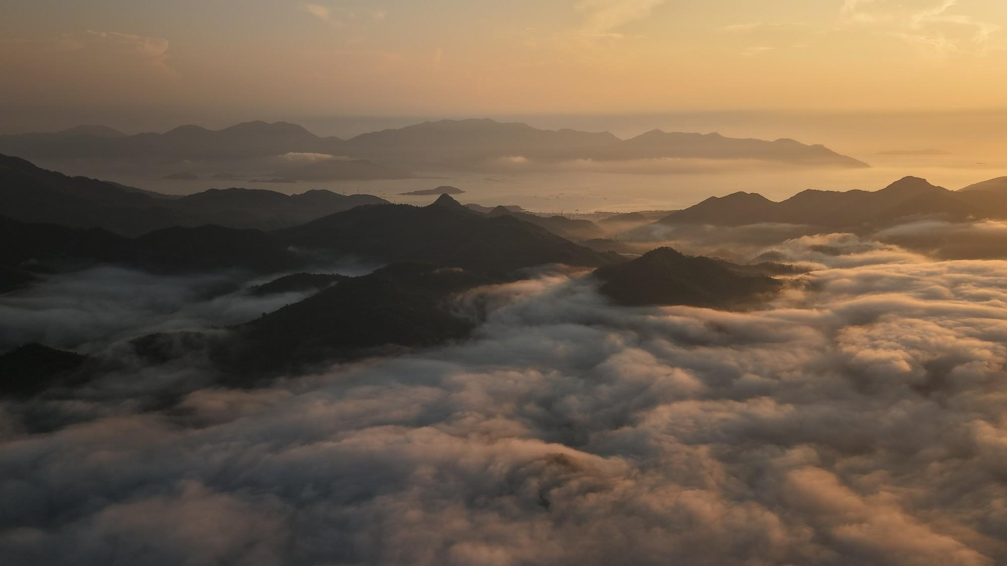 Ở góc nhìn rộng hơn, những đỉnh núi nhô lên giữa biển mây, phía xa là vùng biển Nha Trang. Núi, mây và biển nối tiếp nhau thành nhiều lớp trong ánh nắng sớm.