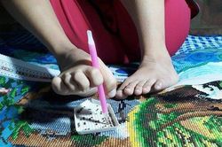 Cô gái khuyết tật dùng chân đính tranh đá thuần thục