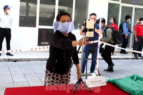 Sau khi rửa tay sát khuẩn, người dân tiến vào khu vực bố trí sẵn điện thoại thông minh, tháo khẩu trang và ấn nút để nhận diện khuôn mặt. Nếu máy nhận diện đúng người dân cần được hỗ trợ sẽ có thông báo "Thành công". Người dân có thể tiến sang khu vực nhận gạo. Ảnh: Giang Thanh