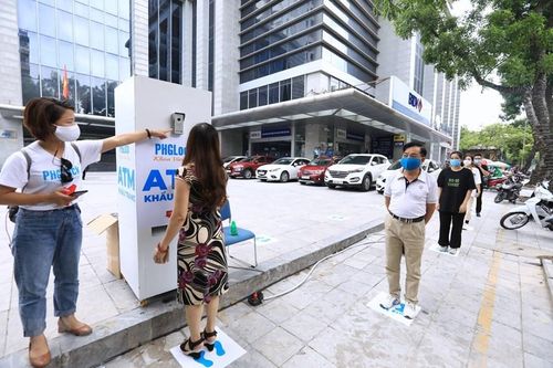 Người dân xếp hàng giãn khoảng cách đến lấy khẩu trang tại cây ATM phát khẩu trang miễn phí trên phố Lạc Trung, Hà Nội. (Ảnh: Thành Đạt/TTXVN)