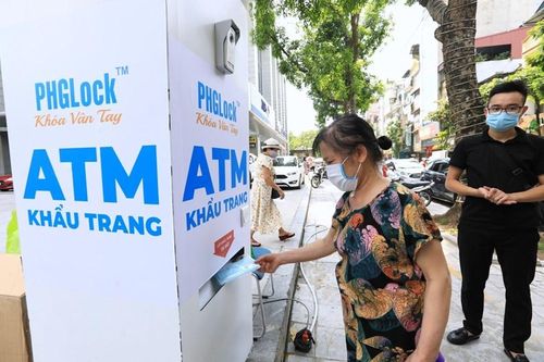 Người dân xếp hàng giãn khoảng cách đến lấy khẩu trang tại cây ATM phát khẩu trang miễn phí trên phố Lạc Trung, Hà Nội.(Ảnh: Thành Đạt/TTXVN)