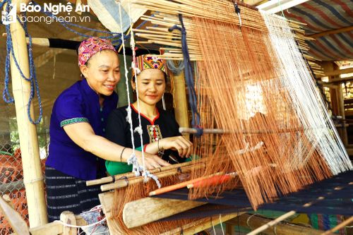 Chị Lô Thị Mai - Tổ trưởng tổ dệt thổ cẩm bản Na (bên trái), cho biết: Ban quản lý Tổ có 3 người, chuyên lo các khâu từ thiết kế, tiếp nhận mẫu mã mới; đồng thời tính toán chi phí về sợi, ngày công; lo nguyên liệu đầu vào; liên kết để tiêu thụ sản phẩm và phổ biến cho từng thành viên trong tổ dệt các sản phẩm theo yêu cầu của thị trường. Ảnh: Nguyên Nguyên