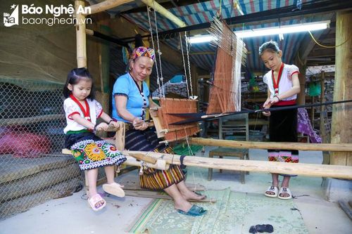  Bà Lô Thị Mai (áo xanh) có 2 cháu gái. Bé lớn là Lô Thị Yến Hương sắp vào lớp 4, bé sau Lô Thị Yến Vi chuẩn bị lên lớp 2. Những tháng Hè vừa qua là quãng thời gian các bé được vui đùa thỏa thích, nhưng bà cũng không quên việc dạy các cháu nghề canh cửi vốn đã trở thành nghề truyền thống của cộng đồng người Thái ở bản Na. Ảnh: Đình Tuyên 