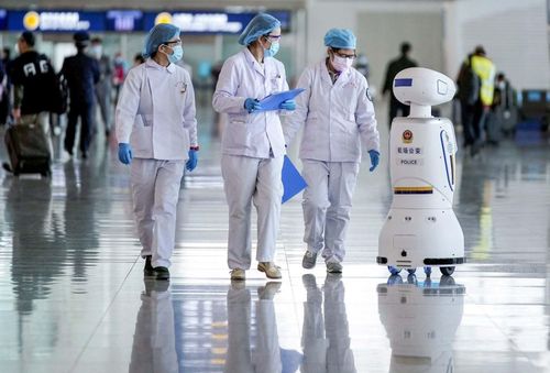 Nhân viên y tế và robot của cảnh sát Trung Quốc cùng làm việc tại sân bay quốc tế Vũ Hán (Trung Quốc). Ảnh: Reuters.