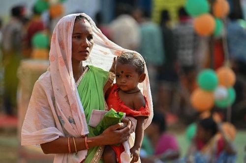 Một cử tri bế con chờ bỏ phiếu bên ngoài một điểm bỏ phiếu ở làng Dugeli, quận Dantewada, bang Chhattisgarh.