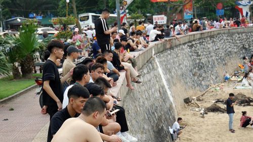Nhiều người ngồi trên bờ kè chờ người thân tắm biển.