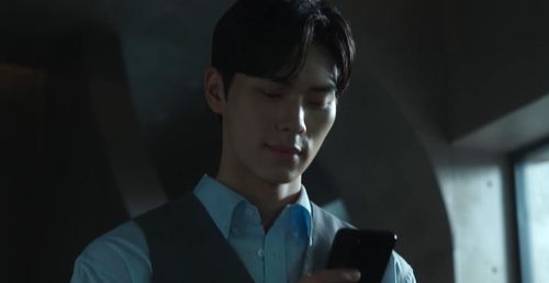 Kang Ha (Lee Chae Min) vừa cười vừa bước đi đắc ý ở hành lang và nhìn vào điện thoại.