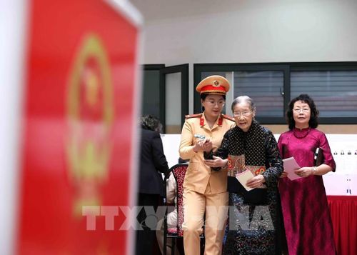 Lực lượng Cảnh sát giao thông cùng con cháu hỗ trợ cử tri Đoàn Thị Thuận, 101 tuổi đến bầu cử tại khu vực bỏ phiếu số 8, phường Ba Đình, thành phố Hà Nội. Ảnh: An Đăng - TTXVN 