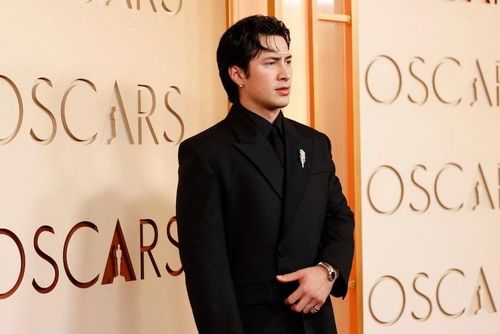  Ngôi sao Heated Rivalry Hudson Williams lịch lãm với bộ tuxedo Balenciaga màu đen thanh lịch, kết hợp áo sơ mi cổ đứng cùng tông và ghim cài áo. Năm qua, anh trở thành hiện tượng toàn cầu sau khi xuất hiện trong bộ phim của đạo diễn Jacob Tierney. Ảnh: Reuters. 