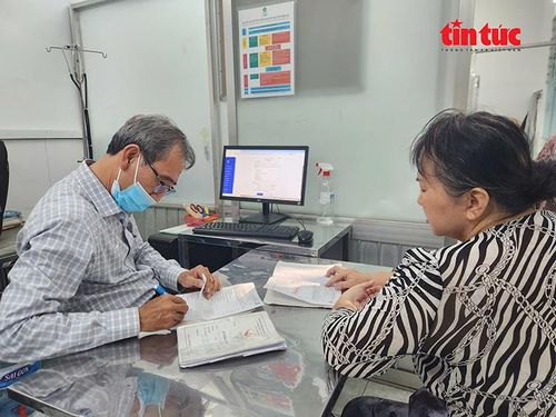 Bác sĩ Tạo xem sổ khám bệnh và tiến hành kê đơn thuốc cho bệnh nhân.