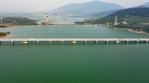 Từ trên cao, cây cầu vươn dài qua mặt nước rộng lớn, kết nối hai bờ giữa không gian núi non và lòng hồ mênh mang. Sự giao thoa giữa đường nét kiến trúc hiện đại với cảnh quan nguyên sơ tạo nên một góc nhìn giàu tính thẩm mỹ - vừa mạnh mẽ, khoáng đạt, vừa mềm mại, nên thơ.