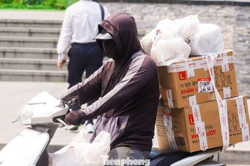 Một shipper trùm kín mít từ đầu đến chân bằng áo khoác, khẩu trang và mũ bảo hiểm có kính râm để bảo vệ cơ thể trước cái nóng oi đầu mùa.