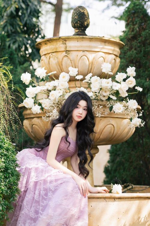 Thiết kế cúp ngực có phần corset xương cá phía trên, bổ sung ren xếp lớp bên dưới. Lọ Lem ứng dụng layout makeup hồng - tím đồng tông, tạo kiểu tóc xoăn lọn quyến rũ.
