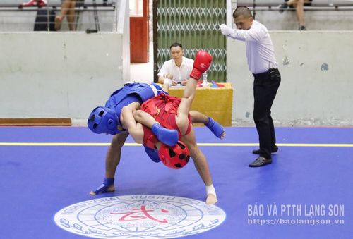 Bên cạnh các đòn đấm, đá, những tình huống ôm, ghì và quật ngã đối thủ cũng là kỹ thuật quan trọng để giành điểm. Hình ảnh hai VĐV đang vật nhau trên sàn đấu cho thấy sự giằng co quyết liệt, khi cả hai cùng tìm cách kiểm soát thế trận, tận dụng sơ hở để thực hiện đòn quật. Những pha xử lý này đòi hỏi sự kết hợp giữa sức mạnh, kỹ thuật và khả năng giữ thăng bằng, đồng thời phản ánh rõ nét tính đối kháng, tốc độ và sự kịch tính đặc trưng của nội dung sanda.