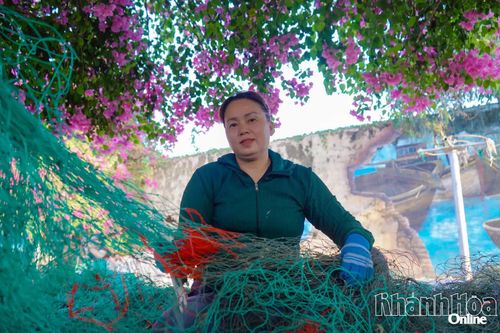 Người dân làng biển Vĩnh Trường đan lưới dưới tán hoa, phía sau là bức tường bích họa cao 4m, dài hơn 300m mang chủ đề “Ngư dân và biển cả”.