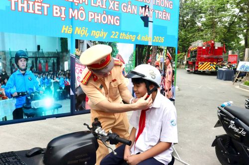 Trung tá Nguyễn Tài Nghĩa, Phó Đội trưởng Đội Tuyên truyền, Phòng Cảnh sát giao thông Hà Nội hướng dẫn học sinh đội mũ bảo hiểm đúng cách. Ảnh: Hồng Nhung