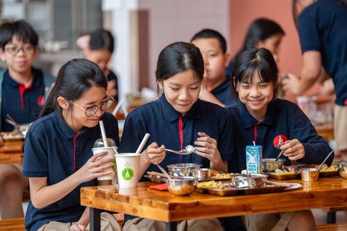  Khi tiếng trống báo hiệu tiết học cuối cùng kết thúc, các học sinh ùa xuống nhà ăn. Khác với các anh chị THCS, học sinh mầm non, tiểu học sẽ xếp hàng điểm danh. Đỗ Linh An (ở giữa), học sinh lớp 6, nói rất thích đồ ăn ở trường bởi đồ ăn phong phú, ngon miệng. Mỗi ngày đi học, An và các bạn đều mong đến giờ nghỉ trưa. Đặc biệt vào thứ sáu, thực đơn thường có những món “đổi vị” nên càng được mong chờ. 