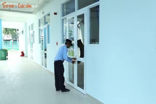 Ghi nhận, bên trong khuôn viên trường, nhiều công nhân đang tất bật dọn dẹp, vệ sinh, tưới cây và lắp đặt trang thiết bị tại các phòng học để chuẩn bị đưa công trình vào vận hành. Trong ảnh, bảo vệ đang kiểm tra lại ổ khóa phòng học.