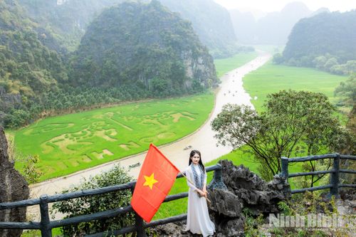 Bạn trẻ lựa chọn trang phục áo dài truyền thống với lá cờ Tổ quốc nổi bật giữa cánh đồng xanh mướt tại Tam Cốc - Bích Động.