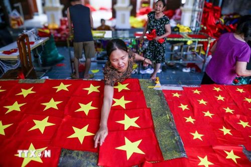 Người thợ kiểm tra lại từng sản phẩm, chỉnh sửa những chi tiết nhỏ nhất để đảm bảo mỗi lá cờ đều đạt chuẩn. (Ảnh: Lê Ngọc/TTXVN phát)
