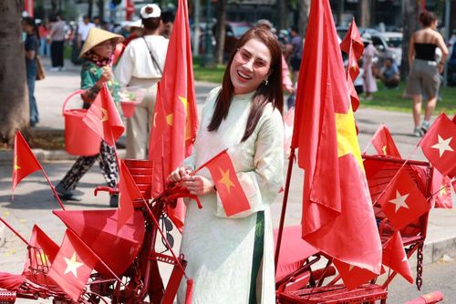 Người phụ nữ chụp ảnh bên chiếc xe trang hoàng nhiều lá cờ đỏ sao vàng.
