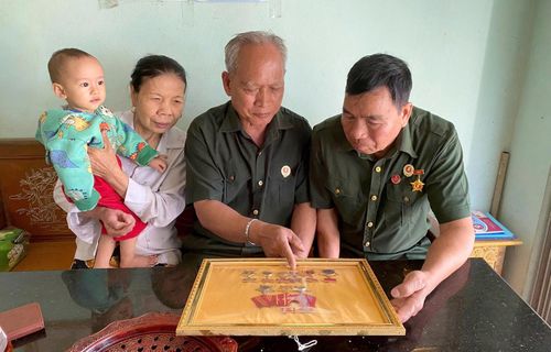 Cựu chiến binh Khuất Việt Vo (ngồi giữa) cùng đồng đội ôn lại kỷ niệm chiến trường qua những kỷ vật lưu giữ tại gia đình.