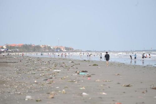 Du khách giữa bãi biển ngập rác, phía xa là những khối nhà của người dân.