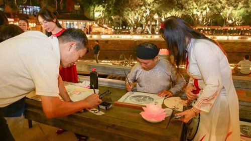 Du khách trải nghiệm viết thư pháp và xin chữ thư pháp. (Ảnh: BẢO LONG)