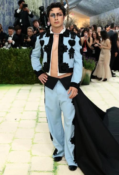 Hudson Williams diện bộ vest Balenciaga màu xanh nhạt được thiết kế riêng với phần đuôi áo dài màu đen. Anh bỏ chiếc áo sơ mi bên trong áo khoác và tạo điểm nhấn thời trang với lớp trang điểm mắt lấy cảm hứng từ “Black Swan” đầy ấn tượng. Ảnh: Getty