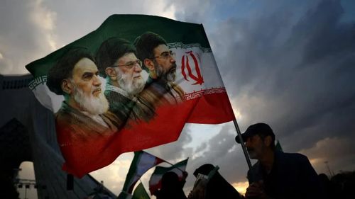 Người dân cầm cờ in hình các nhà lãnh đạo Iran. Ảnh: Reuters