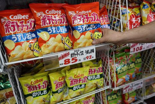  Nhân viên thêm khoai tây chiên Calbee lên kệ tại một cửa hàng chuyên bán bánh kẹo ở Tokyo, Nhật Bản, ngày 12/5. Ảnh: Reuters.