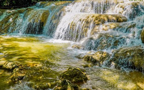 Từ xa, tiếng nước đổ vang vọng giữa núi rừng. Dưới chân thác, nhiều du khách ngồi trên các phiến đá lớn, ngâm chân trong dòng nước lạnh buốt.