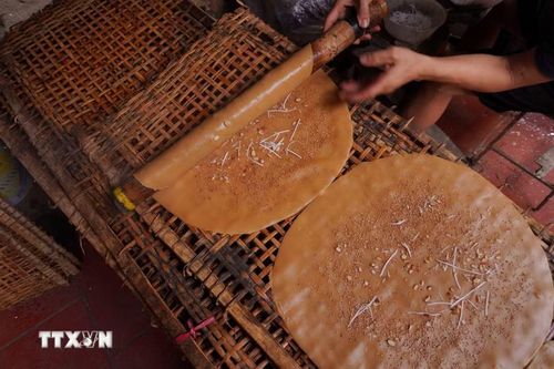 Người thợ tỉ mỉ cuốn bánh vừa tráng lên phên tre; phía trên mặt bánh đã được rải đều vừng, lạc và dừa nạo nức tiếng thơm bùi. (Ảnh: Hà Anh/TTXVN phát)