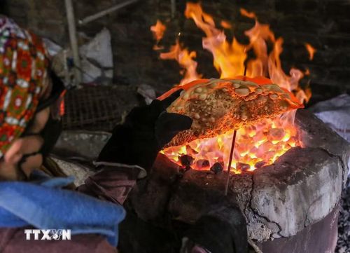 Để có những chiếc bánh đa dừa nướng thơm ngon, người thợ làng Thổ Hà phải ngồi bên bếp than hồng rực lửa hàng giờ đồng hồ, nhanh tay xoay đều để bánh chín vàng ruộm, giòn tan mà không bị cháy. (Ảnh: Hà Anh/TTXVN phát)