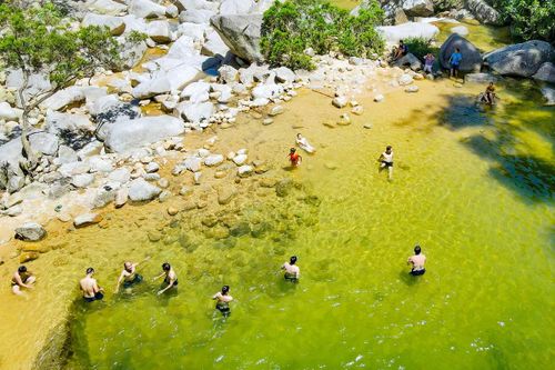 Dưới chân thác, từng nhóm bạn trẻ, gia đình quây quần ngâm mình trong làn nước trong vắt. Tiếng reo hò vang lên mỗi khi dòng nước mát lạnh đổ ập xuống từ các ghềnh đá.