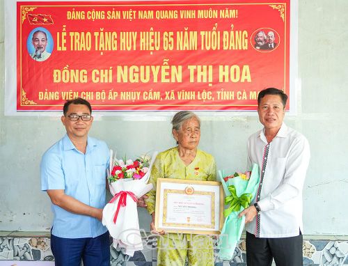  Trưởng Ban Nội chính Tỉnh ủy Cà Mau Trần Hữu Phước và đồng chí Đặng Thành Thương, Bí thư Đảng ủy, Chủ tịch HĐND xã Vĩnh Lộc, trao Huy hiệu 65 năm tuổi Đảng cho đồng chí Nguyễn Thị Hoa.