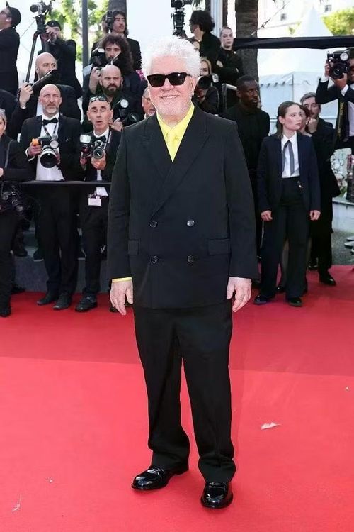 Trong khi phần lớn nam khách mời chọn các bộ suit đen quen thuộc, Pedro Almodóvar tạo điểm nhấn bằng sơ mi và cà vạt vàng chanh nổi bật. Mái tóc bạc cùng kính râm càng khiến diện mạo của đạo diễn khác biệt.