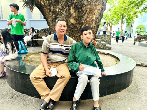  Thí sinh Nguyễn Trân Khiêm (Trường THPT Tây Thạnh) bị khuyết tật nặng hai chân được cha đưa đi thi và ngồi chờ lực lượng thanh niên hỗ trợ đưa lên phòng thi - Ảnh: THANH HÙNG 