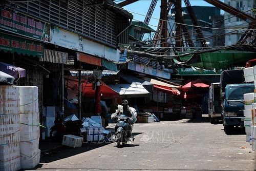Người lao động di chuyển qua khu vực chợ đầu mối trong khung giờ nắng gắt, khi nhiều tuyến phố gần như vắng bóng người đi bộ. Ảnh: Phạm Tuấn Anh/TTXVN