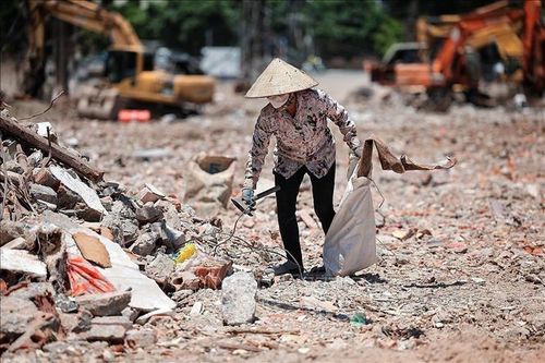 Một phụ nữ thu gom phế liệu giữa bãi đất, công trình ngổn ngang dưới nền nhiệt cao. Ảnh: Phạm Tuấn Anh/TTXVN