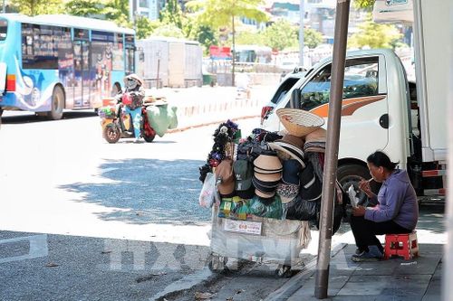 Một người bán hàng rong tranh thủ ngồi nghỉ, ăn vội bữa trưa bên vỉa hè dưới cái nắng gay gắt giữa Hà Nội ngày 25/5. Ảnh: Phạm Tuấn Anh - TTXVN