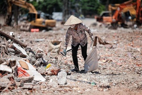 Một phụ nữ thu gom phế liệu giữa bãi đất, công trình ngổn ngang dưới nền nhiệt cao. Ảnh: Phạm Tuấn Anh - TTXVN