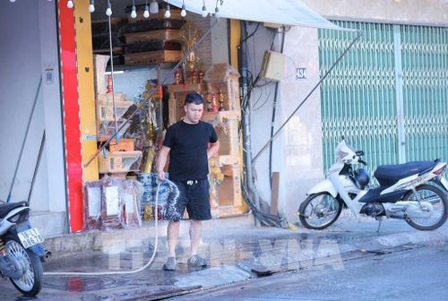 Một người dân trên đường Trương Định xịt nước trước cửa nhà để giảm nhiệt. Ảnh: Hoàng Hiếu - TTXVN