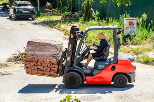 Nắng “cháy da cháy thịt”, người công nhân lái xe nâng vẫn miệt mài vận chuyển những kiện gạch nặng nề tại công trường. Chiếc nón lá truyền thống trở thành “vũ khí” che nắng thô sơ nhưng không thể thiếu giúp họ chống chọi lại cái oi bức cực hạn của ngày hè.