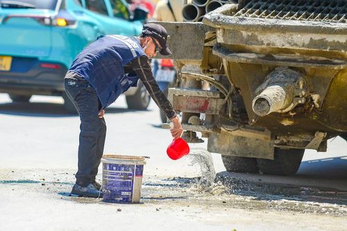 Giữa cái nắng như thiêu như đốt trên 40 độ C, một người công nhân đổ bê tông phải liên tục dùng gáo dội nước để làm mát và làm sạch khu vực họng xả của xe trộn. Sức nóng hầm hập phả ra từ mặt đường nhựa kết hợp với nhiệt độ ngoài trời khiến công việc chân tay vốn đã nặng nhọc nay lại càng thêm phần kiệt sức.