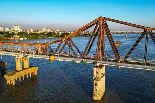 Góc máy trên cao cận cảnh nhịp vòm thép chính của cầu Long Biên. Các phao tiêu cảnh báo đường thủy ở chân trụ cầu được sơn sửa lại rõ ràng, đảm bảo an toàn cho các phương tiện di chuyển trên sông Hồng.