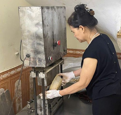 Bà Nguyễn Thị Nhiên đưa khuôn bỏng vào máy ép, công đoạn tạo hình cho những thanh bỏng Chủ truyền thống của đất Cổ Loa. Ảnh:MK