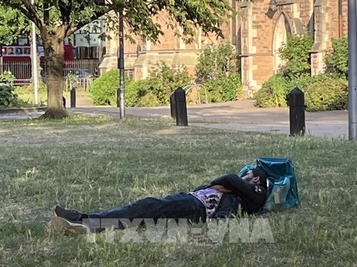 Dưới cái nắng gay gắt, trên bãi cỏ trước một nhà thờ ở Tây London, một người nằm ngủ thiếp bên chiếc ba lô xanh đặc trưng của nghề giao hàng tại Anh. Ảnh: Hương Giang - PV TTXVN tại Anh 